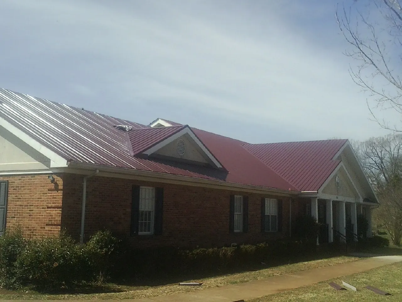 Red metal roof with gabled entries on a long brick building, from a Hail Damage Roof Repair job in Fort Edward