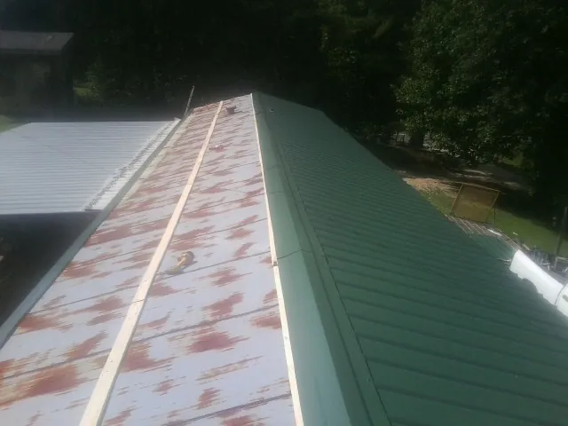 Old rusted panels beside newly installed green metal roofing — Wind Damage Roof Repair by Roofing Brothers in Fort Edward