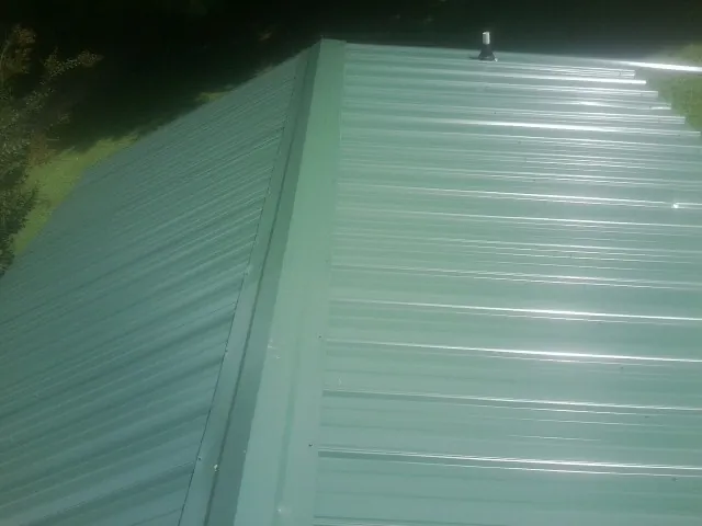 New green metal panels meeting at the ridge of a roof — Flat Roof Repair work by our crew in Fort Edward