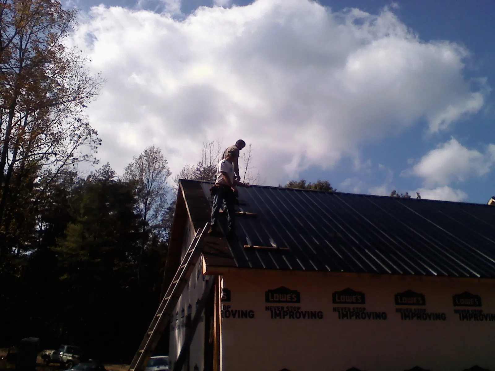 Roofer fastening dark metal panels high against a cloudy sky, from a Roof Inspection job in Fort Edward