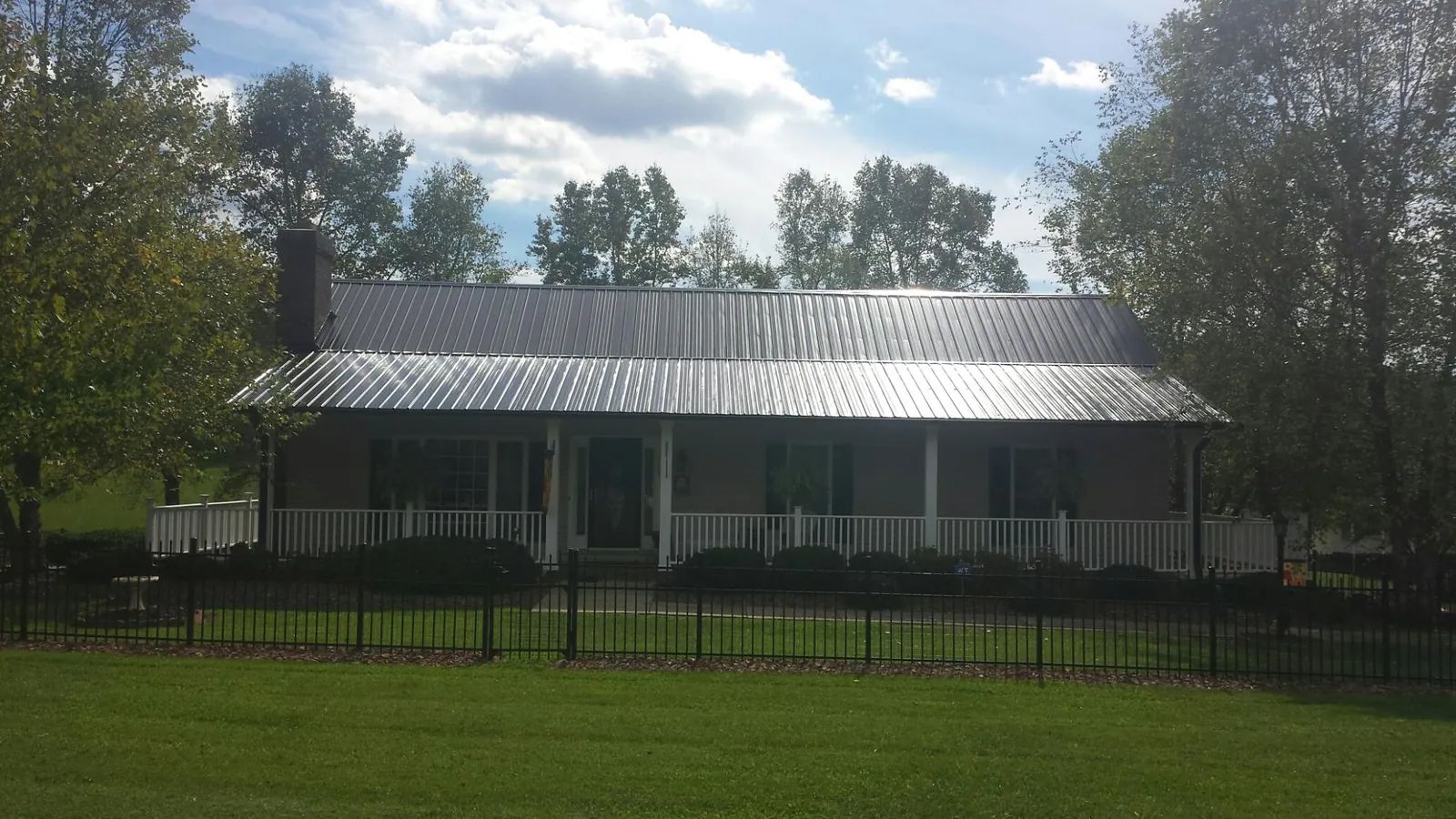 Gray metal roof on a brick ranch with a full width front porch — Gutter Guard Installation work by our crew in Fort Edward