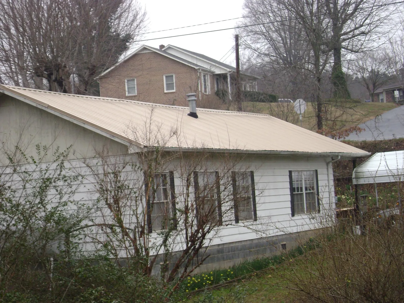 Tan metal roof on a white sided house set into a hillside — Commercial Roofing by Roofing Brothers in Fort Edward