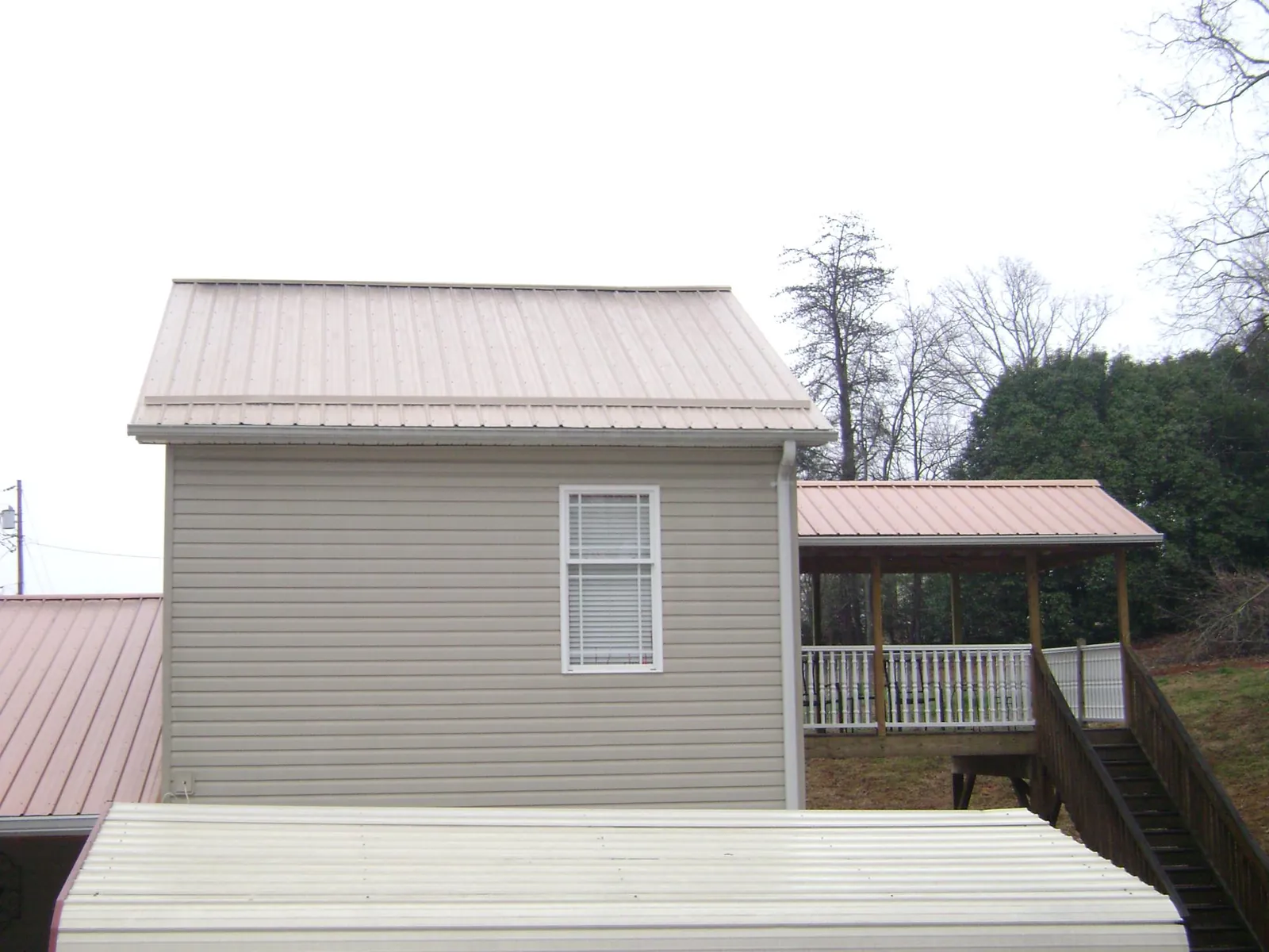 Tan metal roofs on a two story addition and attached porch, from a Roof Replacement job in Fort Edward